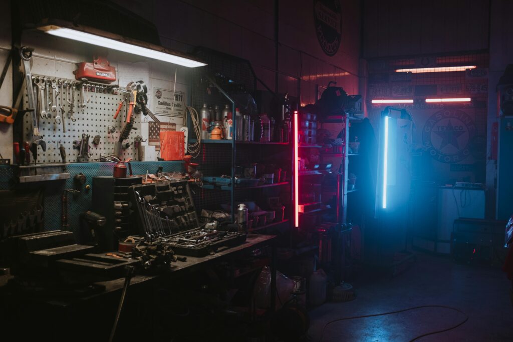 Dimly lit garage featuring neon lights and automotive tools creating a moody ambiance.